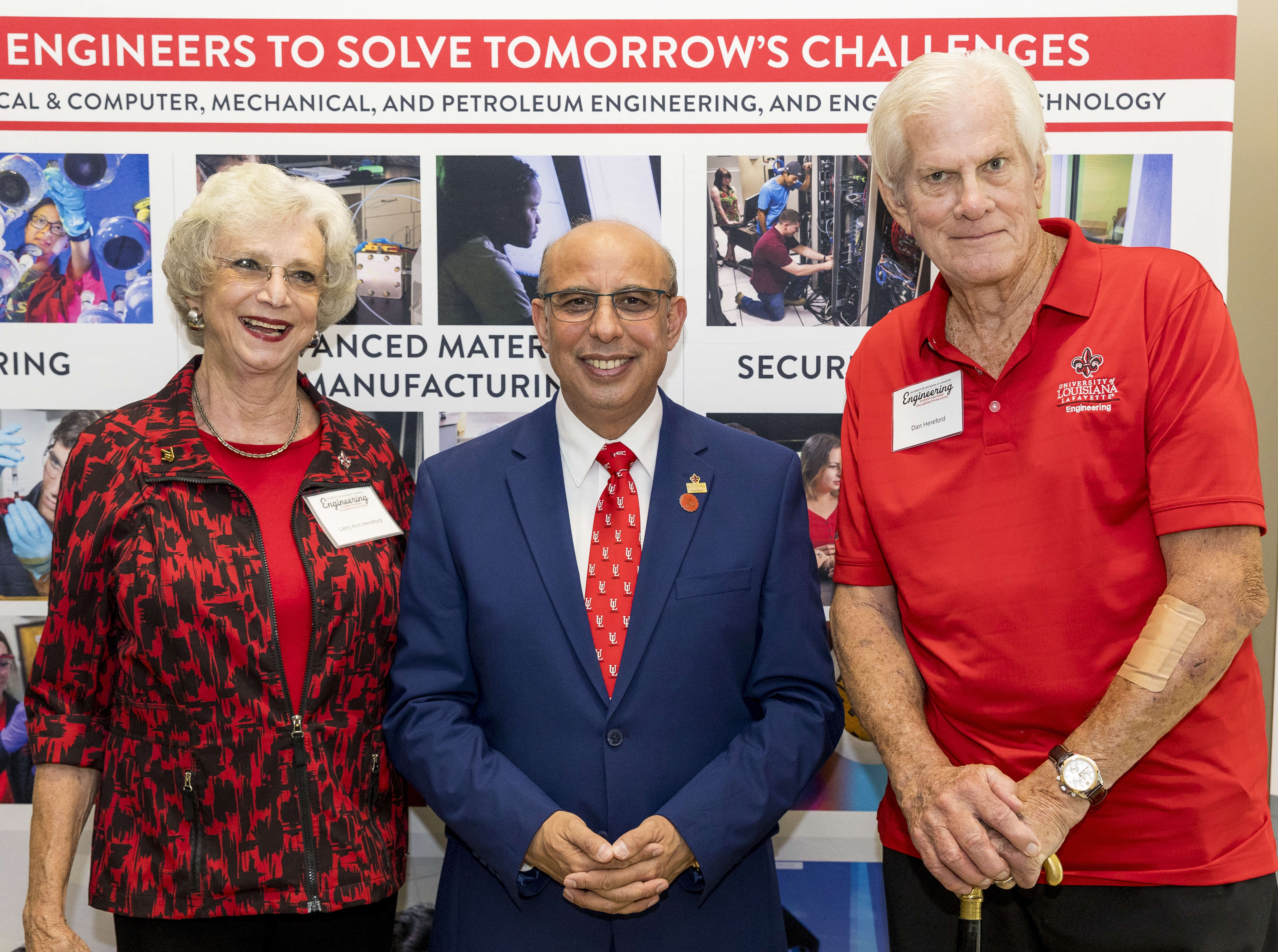 Ms. Larry Ann Hereford, Dean Ahmed Khattab and Mr. Dan Hereford standing in from of an Engineering backdrop entitled Engineering to Solve Tomorrow's Challenges with engineering pictures below.